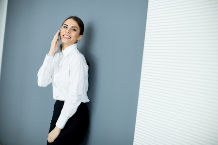 Young woman with mobile phone by the wallの写真素材
