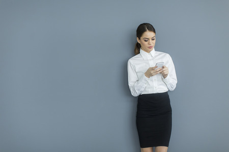 Young woman with mobile phone by the wallの写真素材