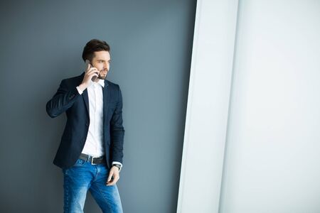 Young man with mobile phone by the grey wallの写真素材