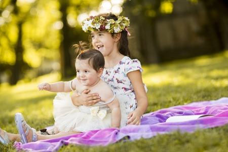 Little girl and baby sitting in the grassの写真素材