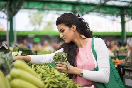 Pretty young woman buying vegetables on the marketの写真素材