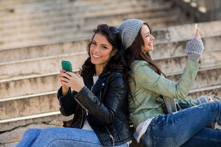 Young women sitting on the stairs with mobile phonesの写真素材