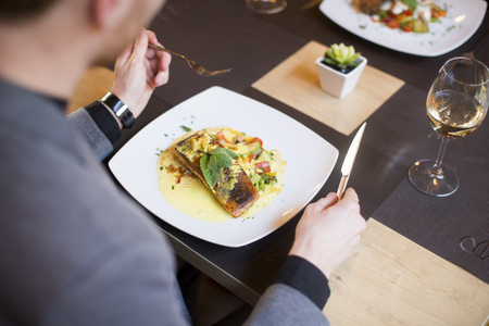 Young man eating grilled salmon with sauce and herbs served at restaurantの写真素材