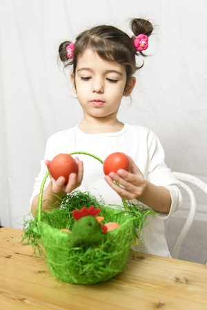 Little girl holding two Easter eggs with a basket with eggs