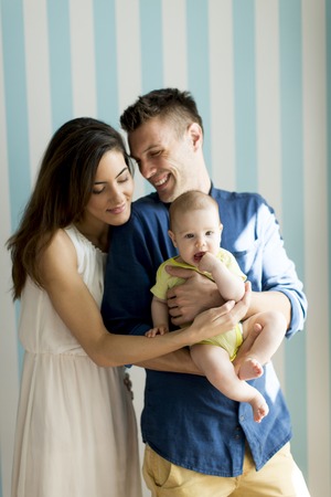 Young family with a baby standing by the wall