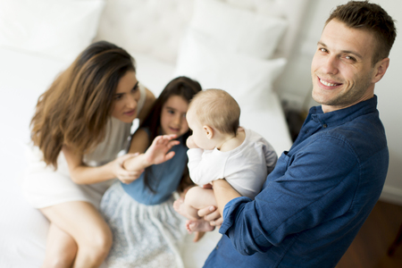Happy young parents sitting on a bed with little girl and babyの写真素材
