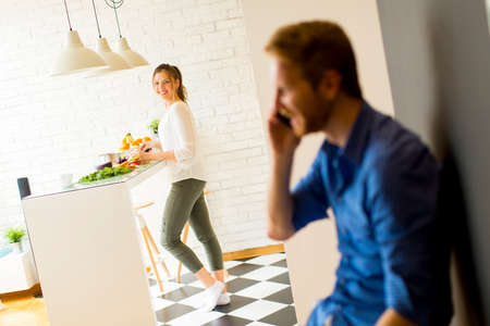 Man on the phone in the kitchen with woman cookingの写真素材