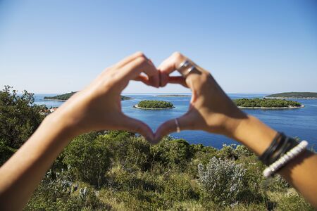 View of the island through the heart shape made from human fingers.の写真素材