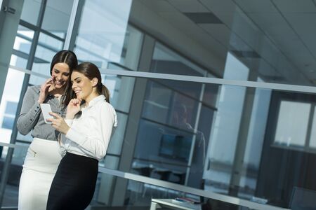 Two businesswomen standing together with the mobile phoneの写真素材