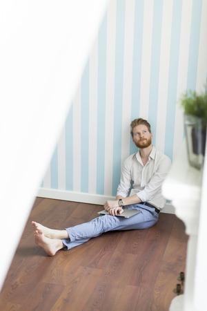 Young redhair man sitting on the floor and working on laptopの写真素材