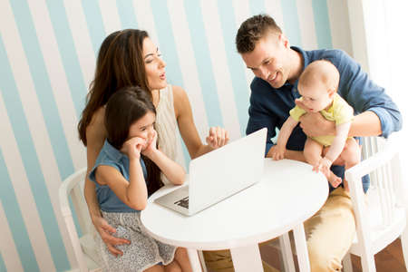 Young parents with daughers by the table with laptop in the roomの写真素材