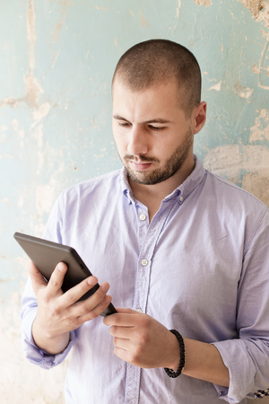 Young man using a tablet by old grunge wallの写真素材