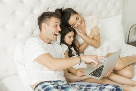 Mother, father and a daughter together on the bed with laptopの写真素材