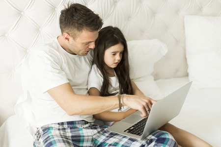 Father and daughter together on the bed with a laptopの写真素材