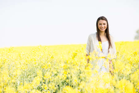 Young woman standing in a field of yellow flowers on a sunny dayの写真素材