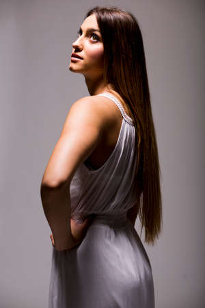 Pretty young woman with long hair in white dress in studioの写真素材