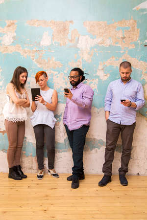 Group of young people standing in front of a grunge wall with a mobile phone handsの写真素材