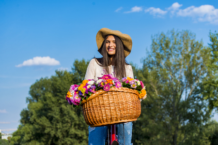 Young girl rides a bicycle with a basket full of flowersの写真素材