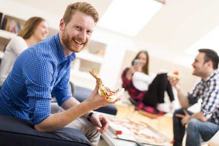 Group of friends eating pizza together at homeの写真素材