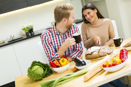 Young man drinking coffee young woman cuts the bread in the kitchenの写真素材