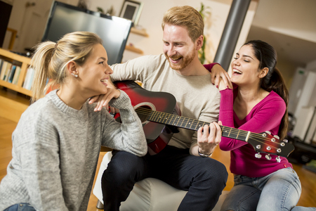 Happy friends playing guitar and listening to music at homeの写真素材