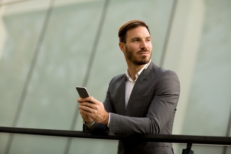 Handsome young bisinessman with mobile phone in front of office building