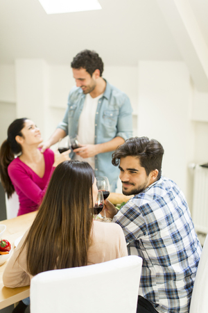 Group of happ young people sitting by the table eating and drinking red wineの写真素材