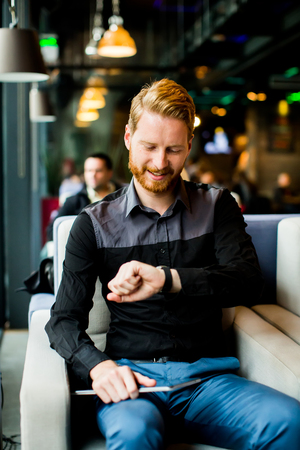 Young redhair man sitting in cafe and holding tablet