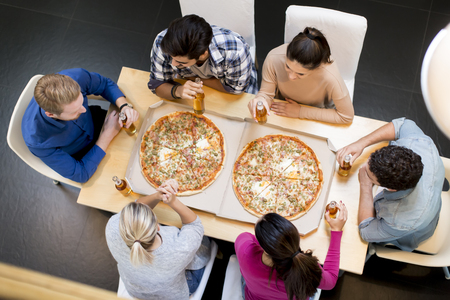 Group of happy young people eating pizza and drinking cider in the modern interiorの写真素材