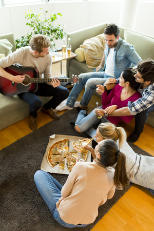 Group of cheerful young people eating pizza in the room and having funの写真素材