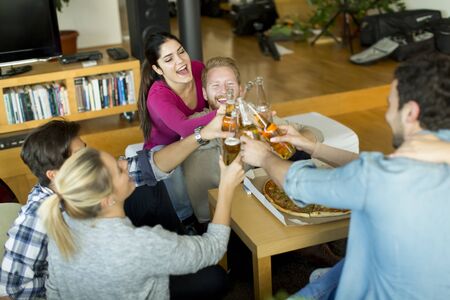 Group of happy young people eating pizza and drinking cider in the modern interiorの写真素材