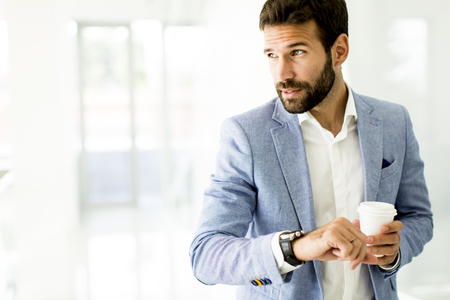 Business man in a business suit , a cup of coffee in a  office building and looking at the clockの写真素材