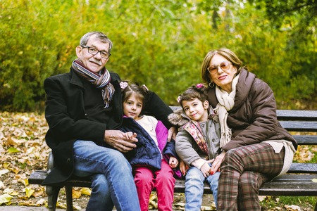 Two little girls sit in the autumn park with her grandparents on a bench