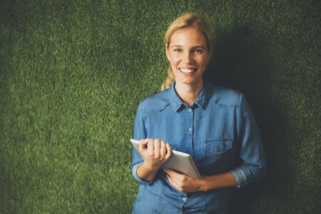 Young woman posing with tablet by green wall