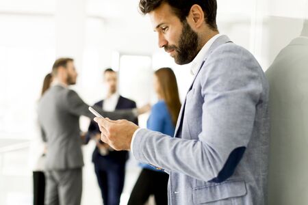 Businessman using mobile phone in office while other business people talking in backgroundの写真素材