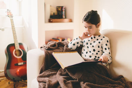 Little girl sitting on sofa and reading bookの写真素材