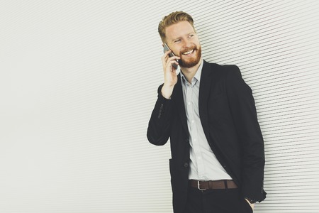 Modern redhair man with mobile phone standing in the office
