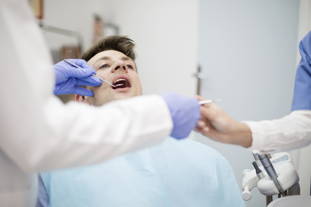 Scared young man at dentist office during teeth checkupの写真素材