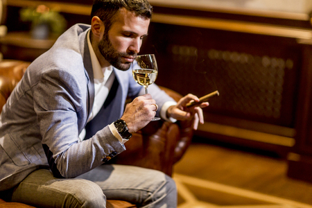 Young man tasting white wine and smoking cigarの写真素材
