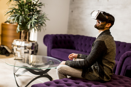 Bearded young man wearing virtual reality goggles in modern roomの写真素材
