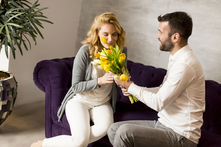 Young woman receiving a gift of  yellow tulips from her husband or partner smiling at himの写真素材