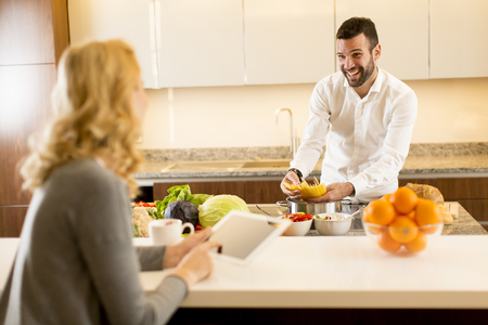 Young man preparing a meal while a young woman sitting and use of tablets in a modern kitchenの写真素材