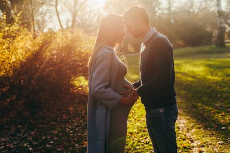 Pregnant woman and her loving man posing at autumn parkの写真素材