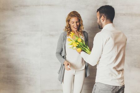 Young woman receiving a gift of  yellow tulips from her husband or partner smiling at himの写真素材