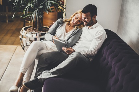 Couple in love sitting on sofa and watching something at tabletの写真素材