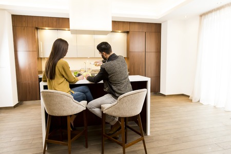 Young couple sitting in the kitchen with his back and drinking white wineの写真素材