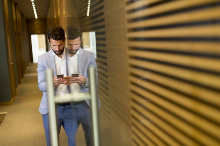 Handsome young businessman with using phone in officeの写真素材