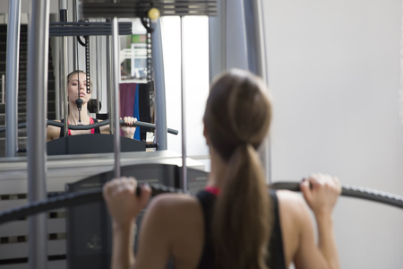 Attractive young woman working out on weight-lifting training machine
