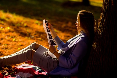 Young pregnant woman sitting under a tree in the autumn park and looking at a snapshot of ultrasoundの写真素材