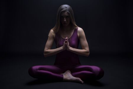 Young woman practicing yoga position in lotus flower, isolated on a dark backgroundの写真素材